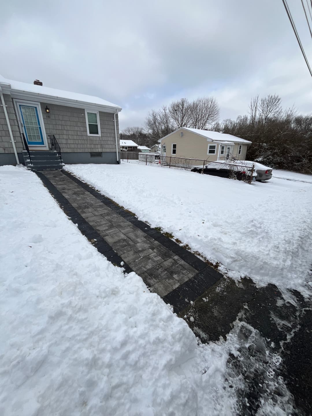 Snow-covered driveway and walkway leading to a blue front door house in winter.