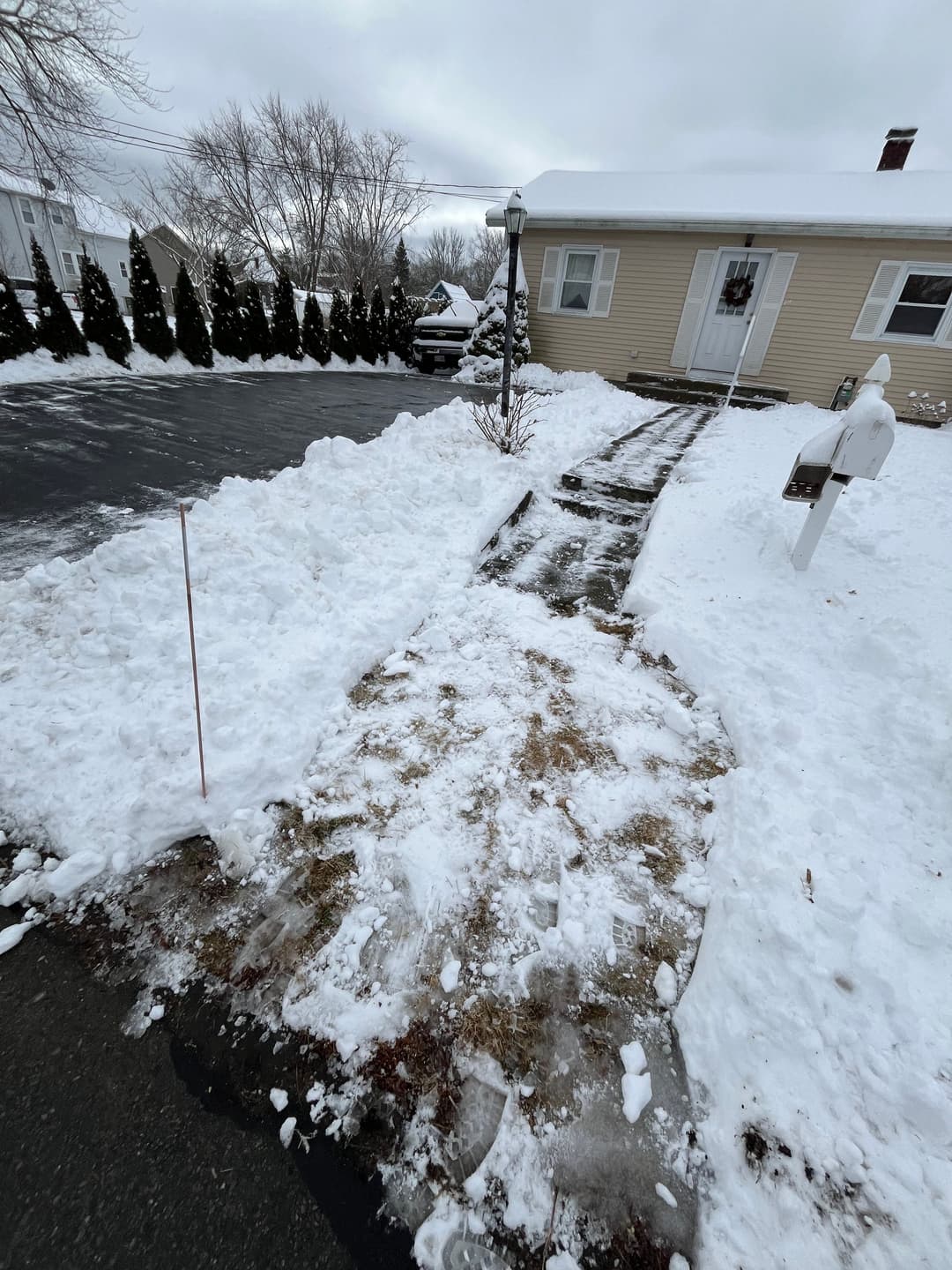 Snow-covered residential driveway and pathway with lamppost and mailbox.