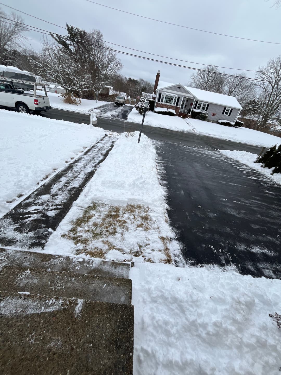 Snow-covered driveway with cleared path, suburban neighborhood in winter.